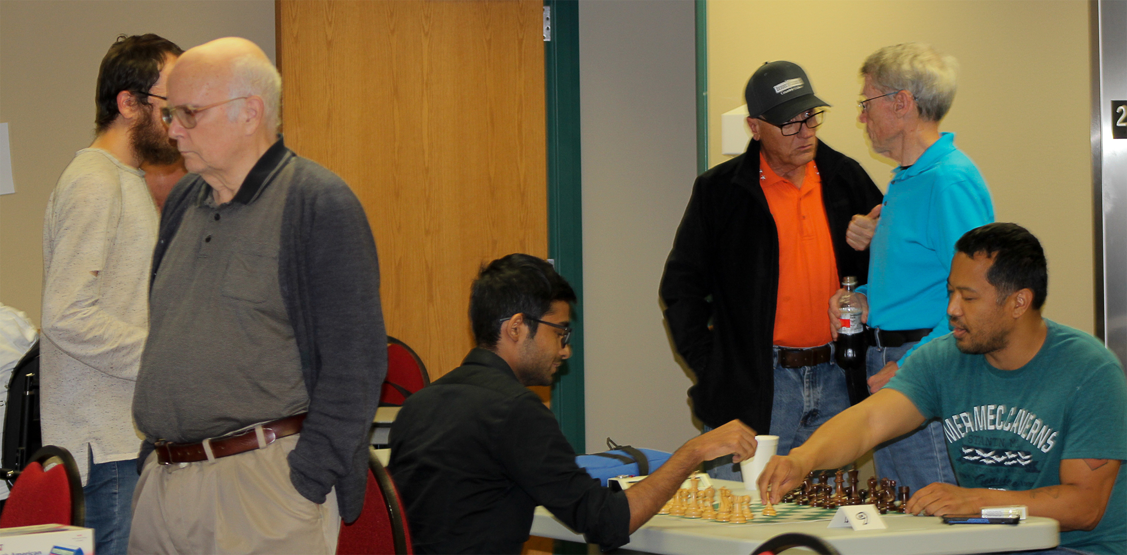 Before the Battle.  Closest to the camera is Oklahoma's Bill Sparks.  Directly behind him is Ishmael Kissinger.  Seated are Texans Ahmad Nazib (wearing black) and Jedwayne Bowser (wearing green).  Standing behind them are Chess Expert Jim Berry (wearing Oklahoma State orange) and Harold Brown (wearing cyan).  Photo by Sheryl McBroom.